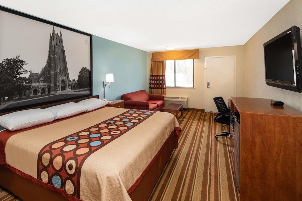 Ein Hotelzimmer mit einem großen Bett, einem Schreibtisch, einem Sessel, einem Fernseher und einem gerahmten Bild an der Wand.
