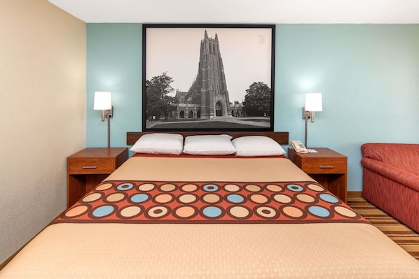 Una habitación de hotel con una cama grande, dos mesitas de noche, un sofá rojo y un cuadro con una catedral en la pared.