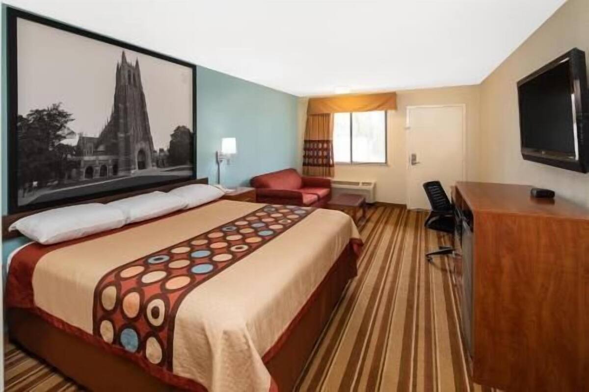 Ein Hotelzimmer mit einem großen Bett, einem Schreibtisch, einem Stuhl, einem Fernseher und einem gerahmten Bild an der Wand.