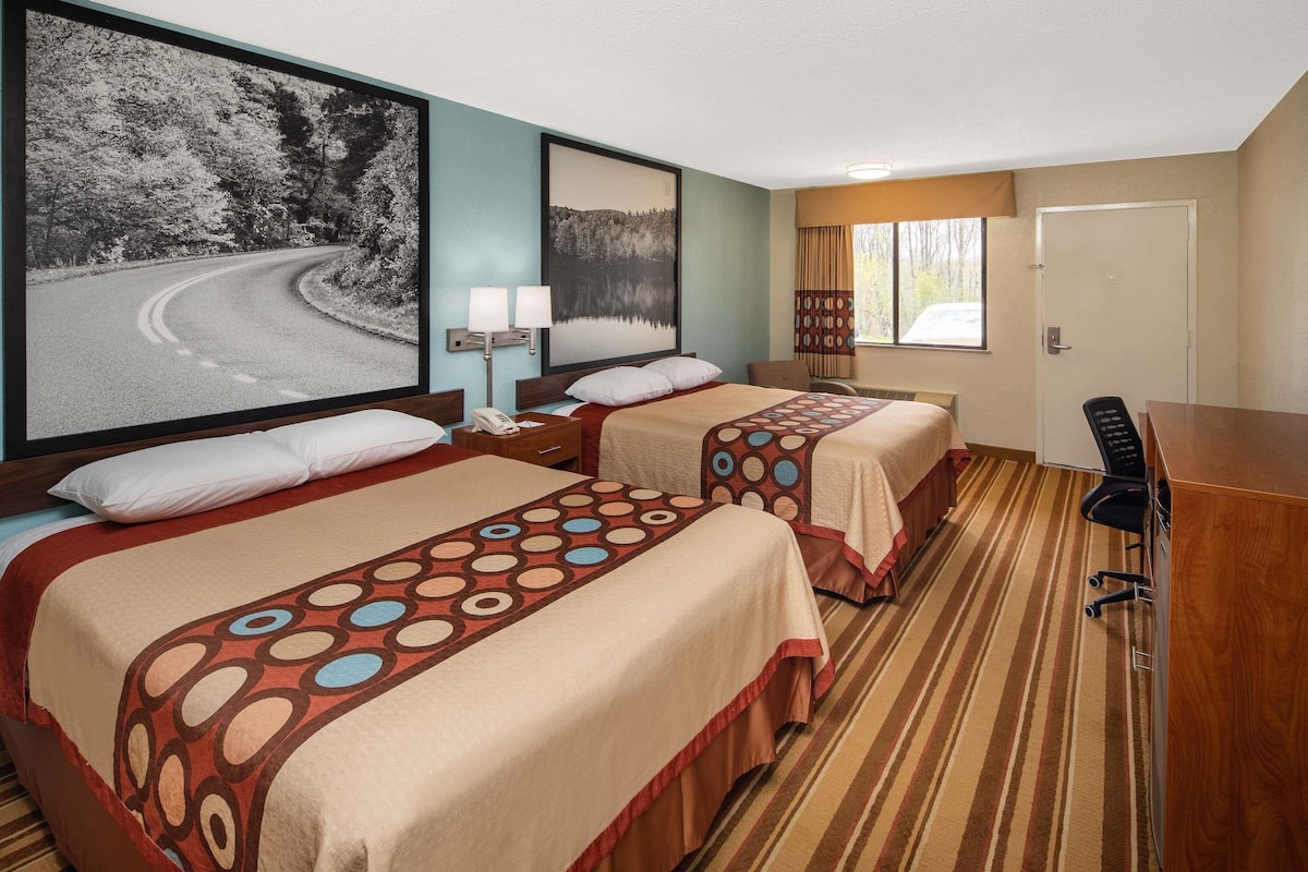 Ein Hotelzimmer mit zwei Betten, einem Schreibtisch, einem Stuhl und einem großen gerahmten Bild einer Straße.