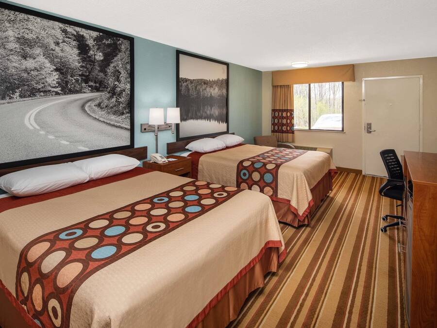 Ein Hotelzimmer mit zwei Betten, einem Schreibtisch, einem Stuhl und einem großen gerahmten Bild einer Straße.