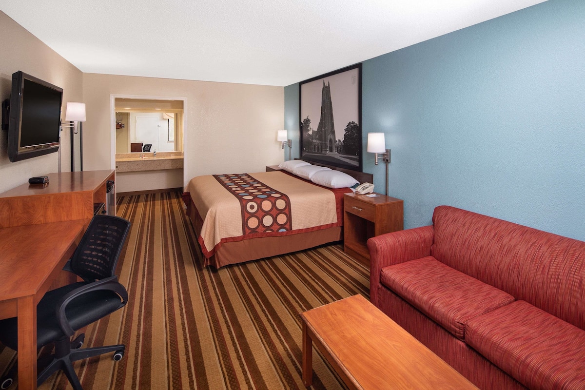 Ein Hotelzimmer mit Bett, Schreibtisch, Stuhl, Sofa, Fernseher und einem Bild an der Wand.