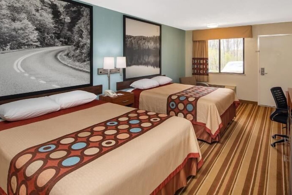 A hotel room with two beds, a desk, a chair, and a large window.