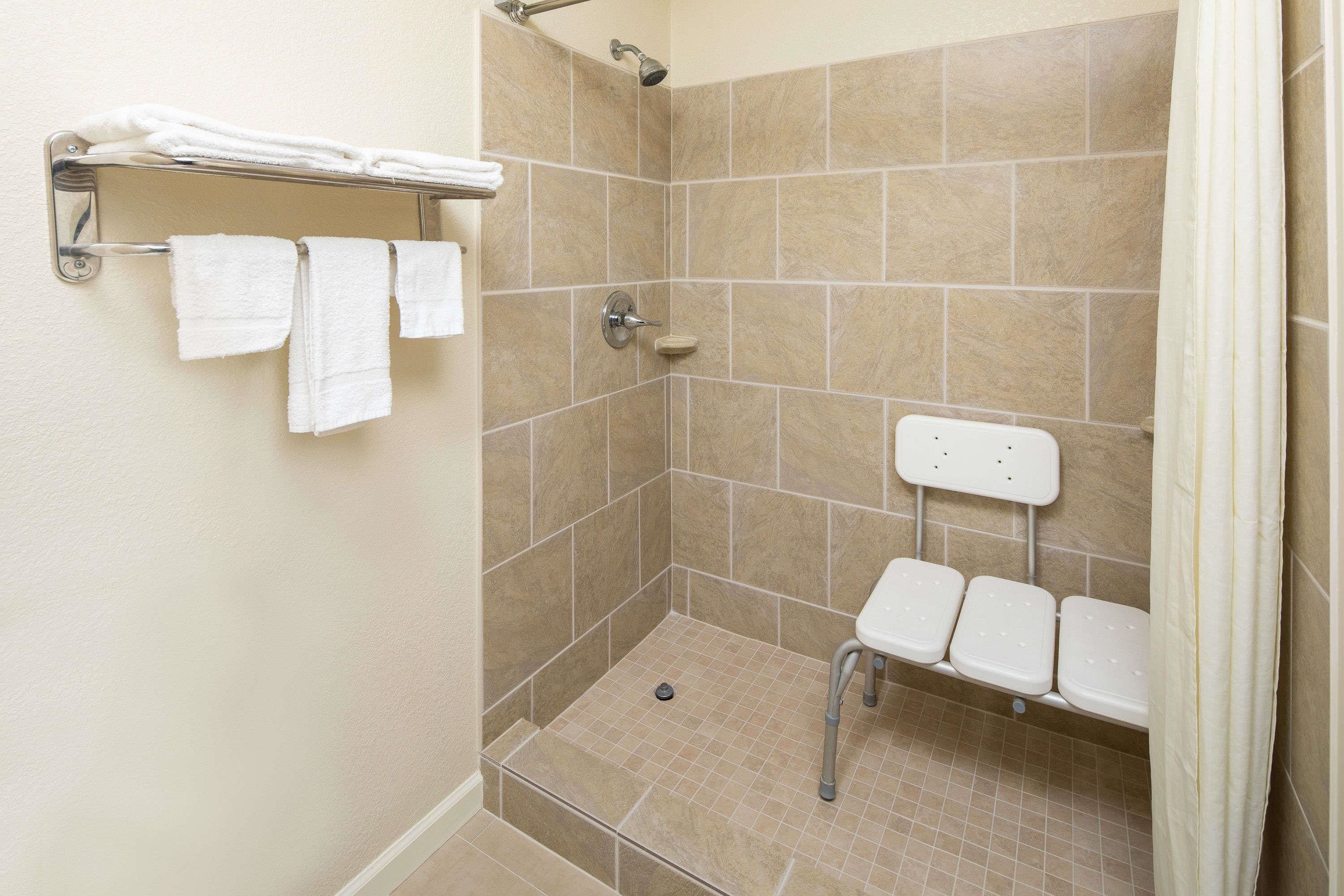 A shower area with a bench, a towel rack, and a showerhead.