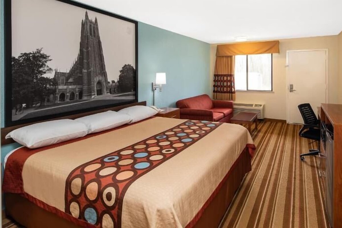 A hotel room with a large bed, a desk, a chair, a TV, and a window with curtains.