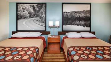 A hotel room with two beds, a nightstand with a lamp, and two framed pictures on the wall.