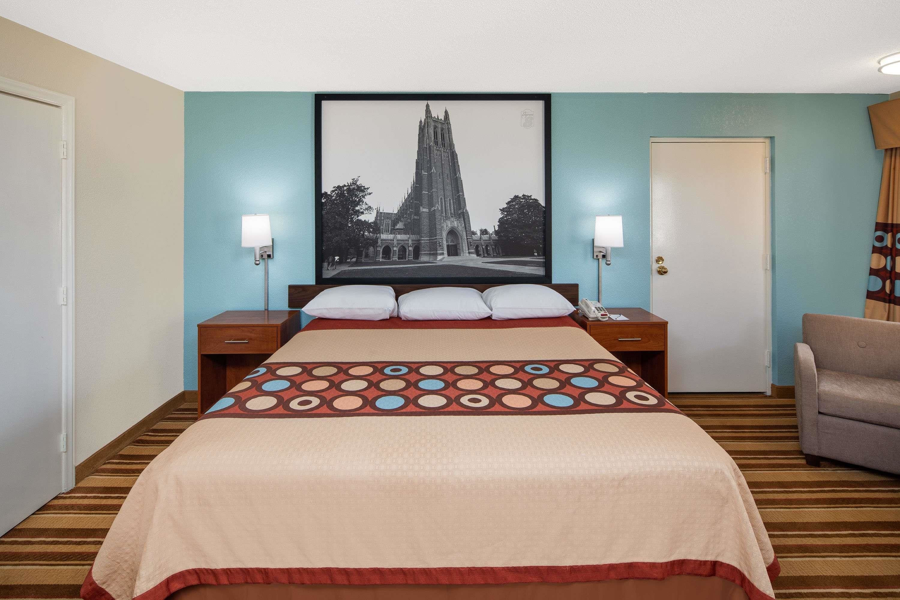 Habitación de hotel con una cama grande, una mesita de noche, una silla y un cuadro en la pared.