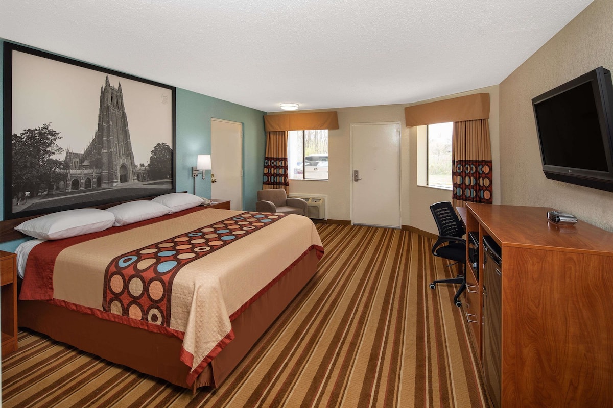 Ein Hotelzimmer mit einem großen Bett, einem Schreibtisch mit Stuhl, einem Fernseher und einem Fenster mit Vorhängen.