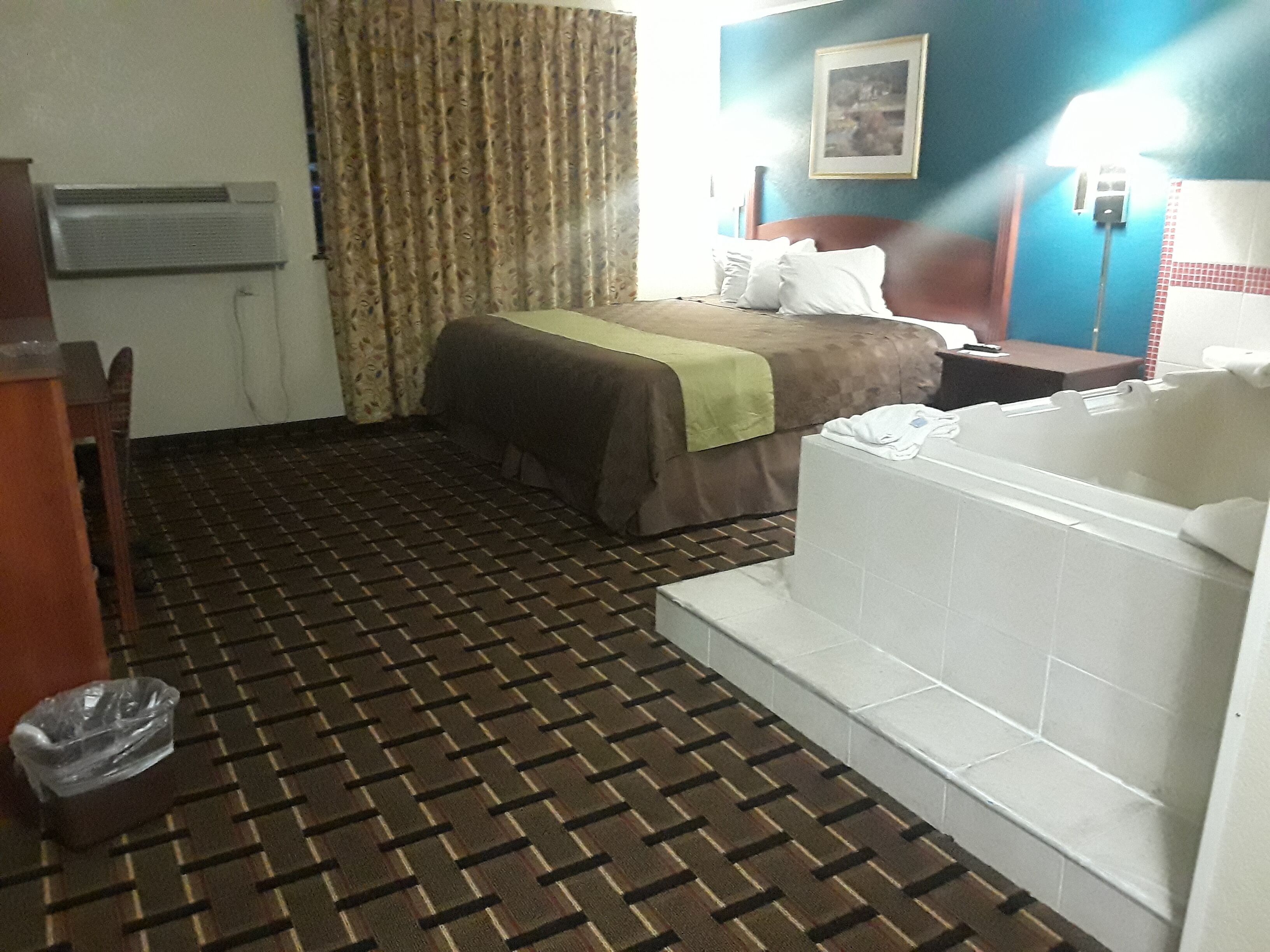Hotelkamer met een bed, een badkamer met bad, een prullenbak en een wandairconditioner.