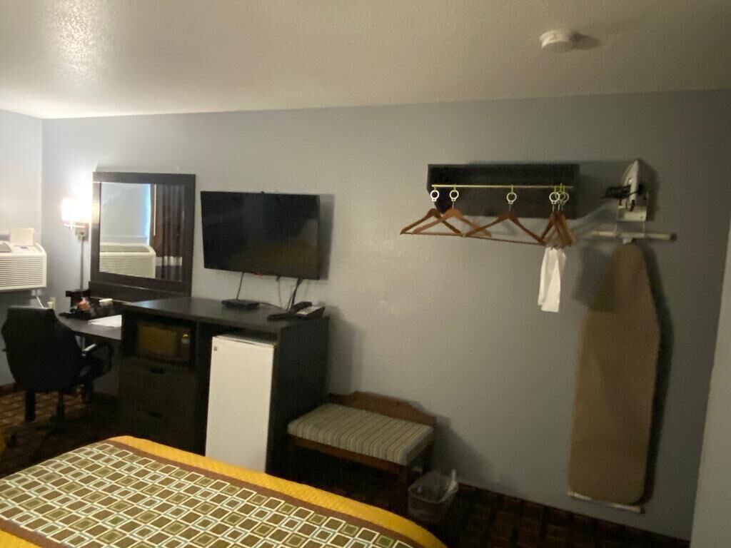 Ett hotellrum med en säng, ett skrivbord med en dator, en tv, en klädställning och en spegel.