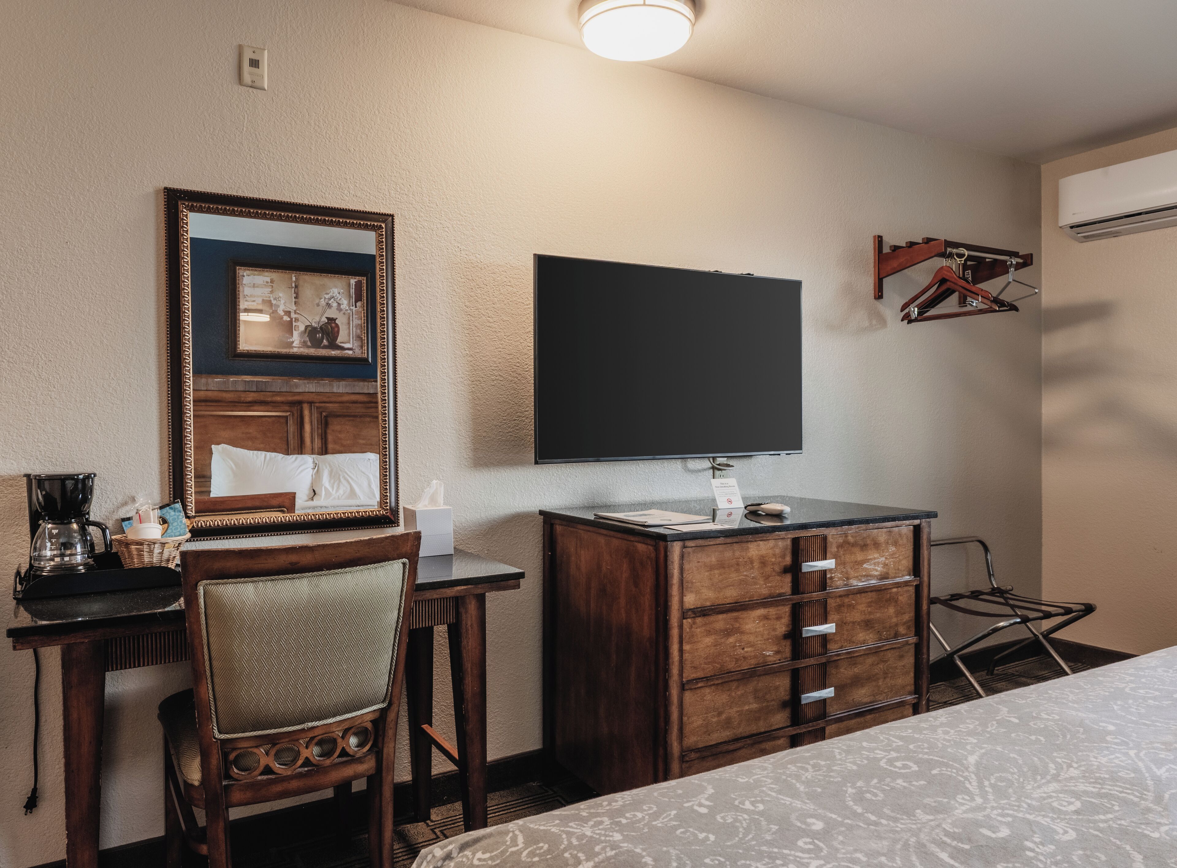 Hotellihuone, jossa on sänky, työp öytä tuolilla, lipasto, televisio ja ilmastointilaite.
