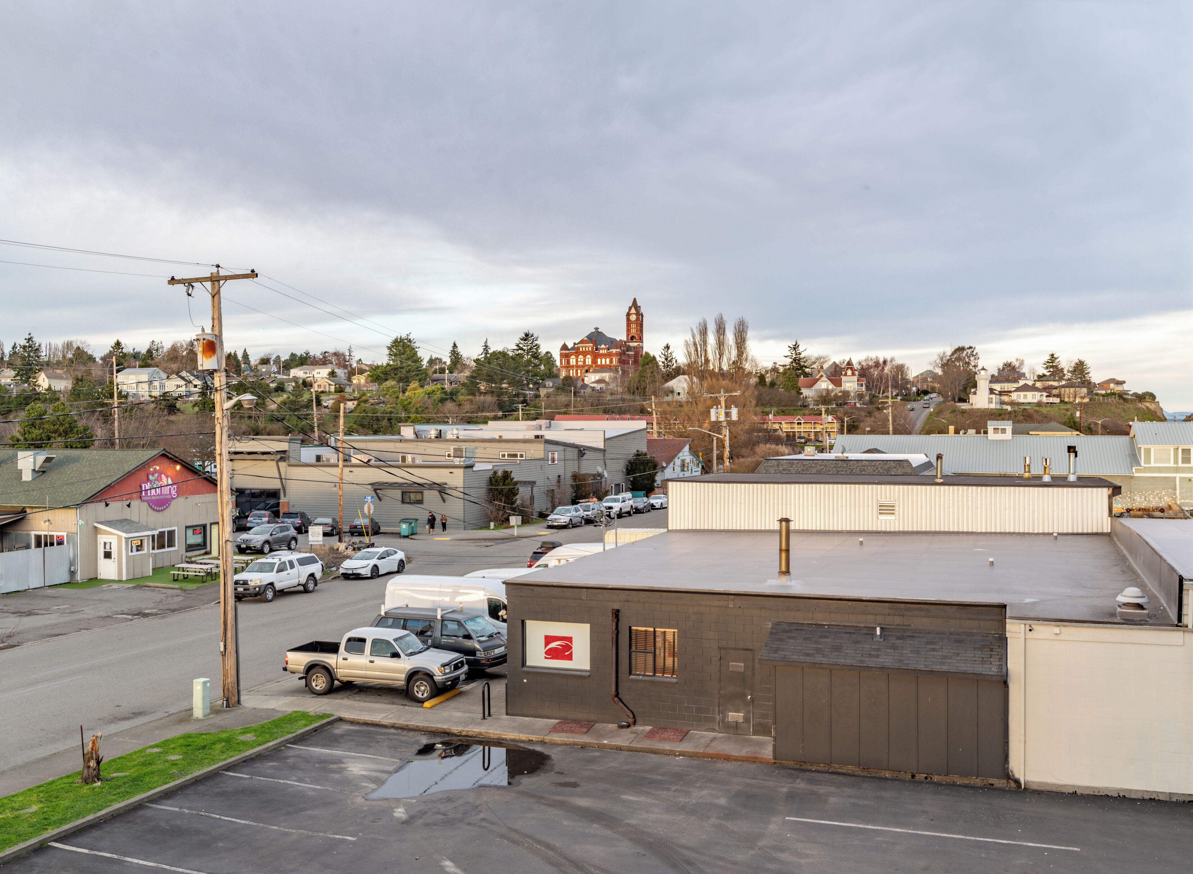 A parking lot with several cars, a building with a red sign, and a distant clock tower.