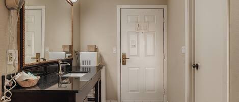 A bathroom with a black countertop, a mirror, a hairdryer, and a white door.
