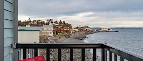 A coastal view from a balcony with a railing, overlooking a rocky shoreline and a row of buildings.