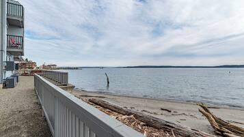 A waterfront view with a wooden pier, a building with balconies, and a calm sea.