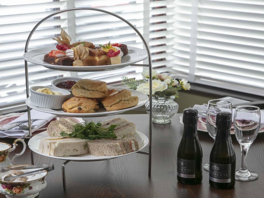 A three-tiered dessert stand with various pastries and sandwiches, two bottles of wine, and a floral-patterned chair.