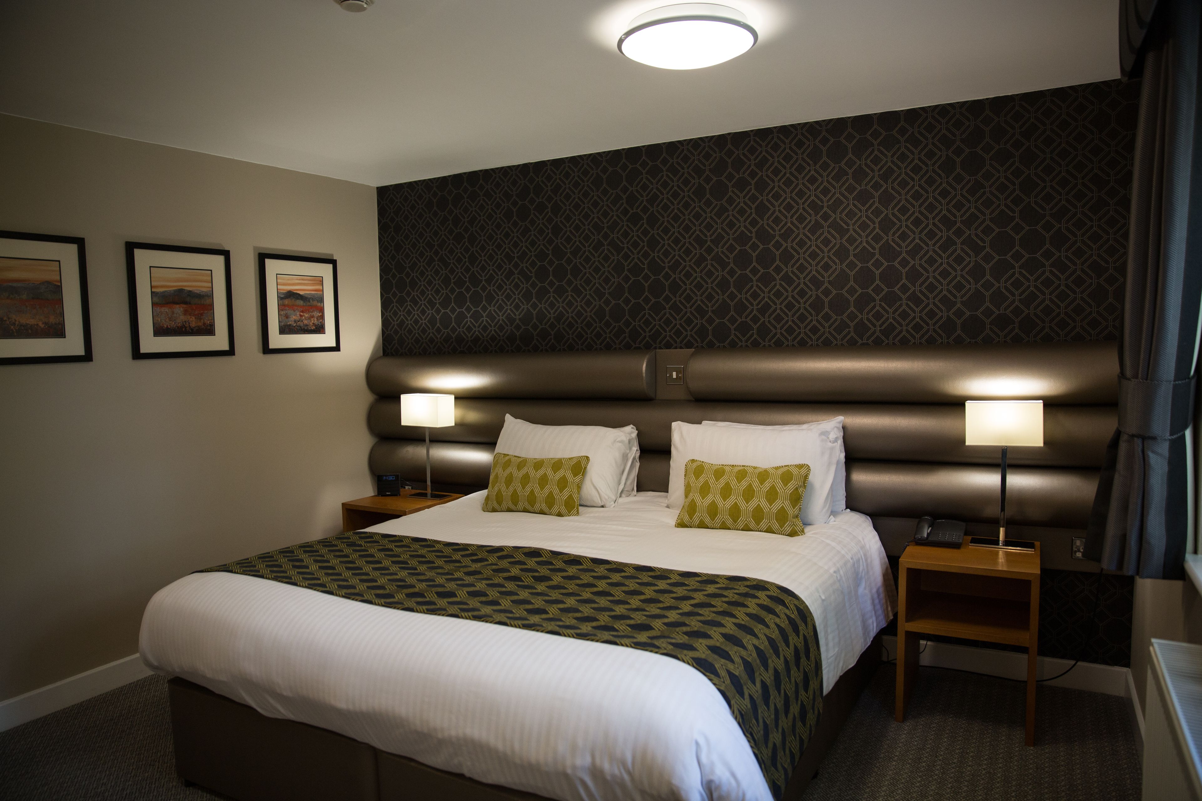 A neatly made bed with a patterned bedspread, two bedside lamps, and a headboard with a geometric pattern.