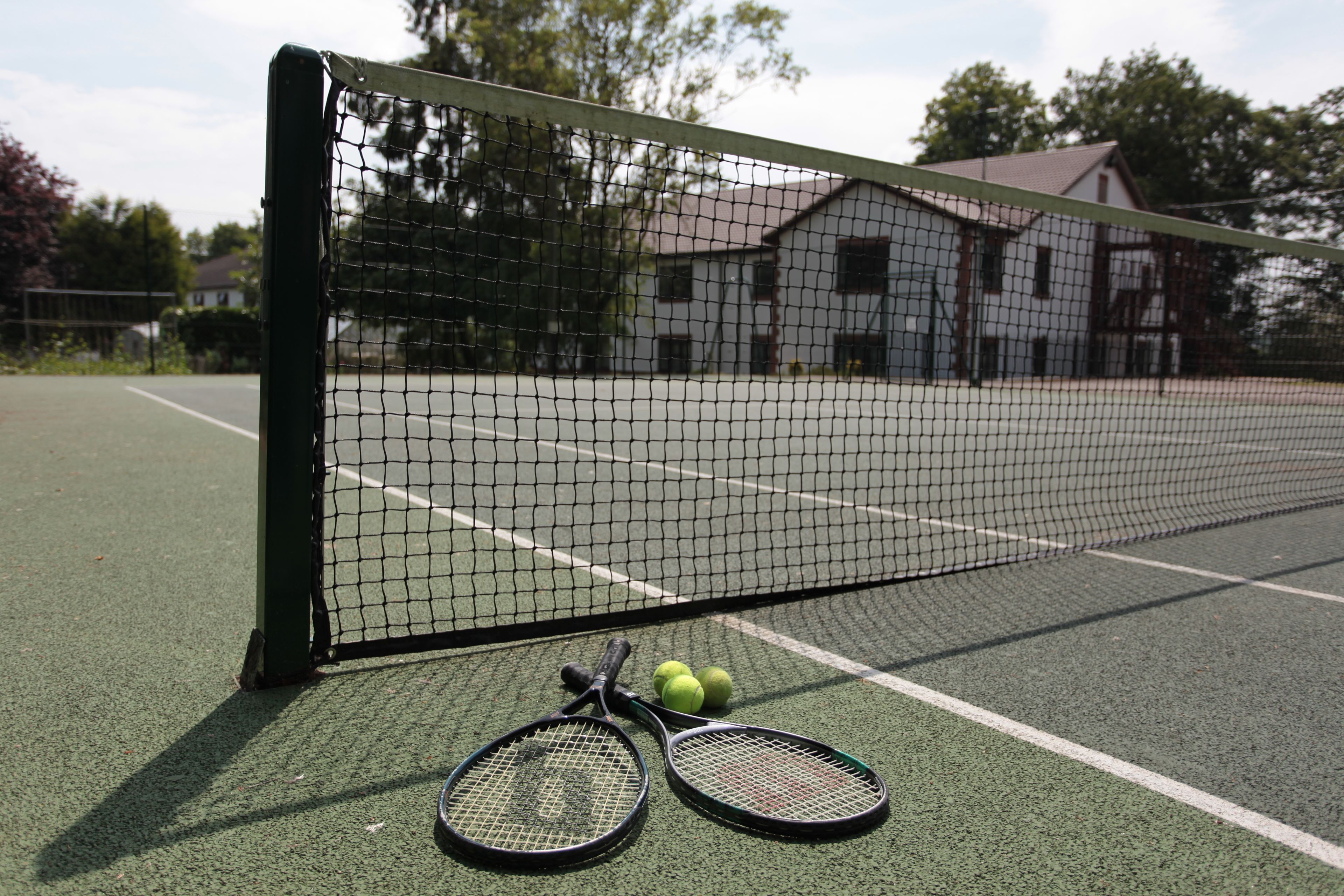 A tennis court with a net, two tennis rackets, and three tennis balls.