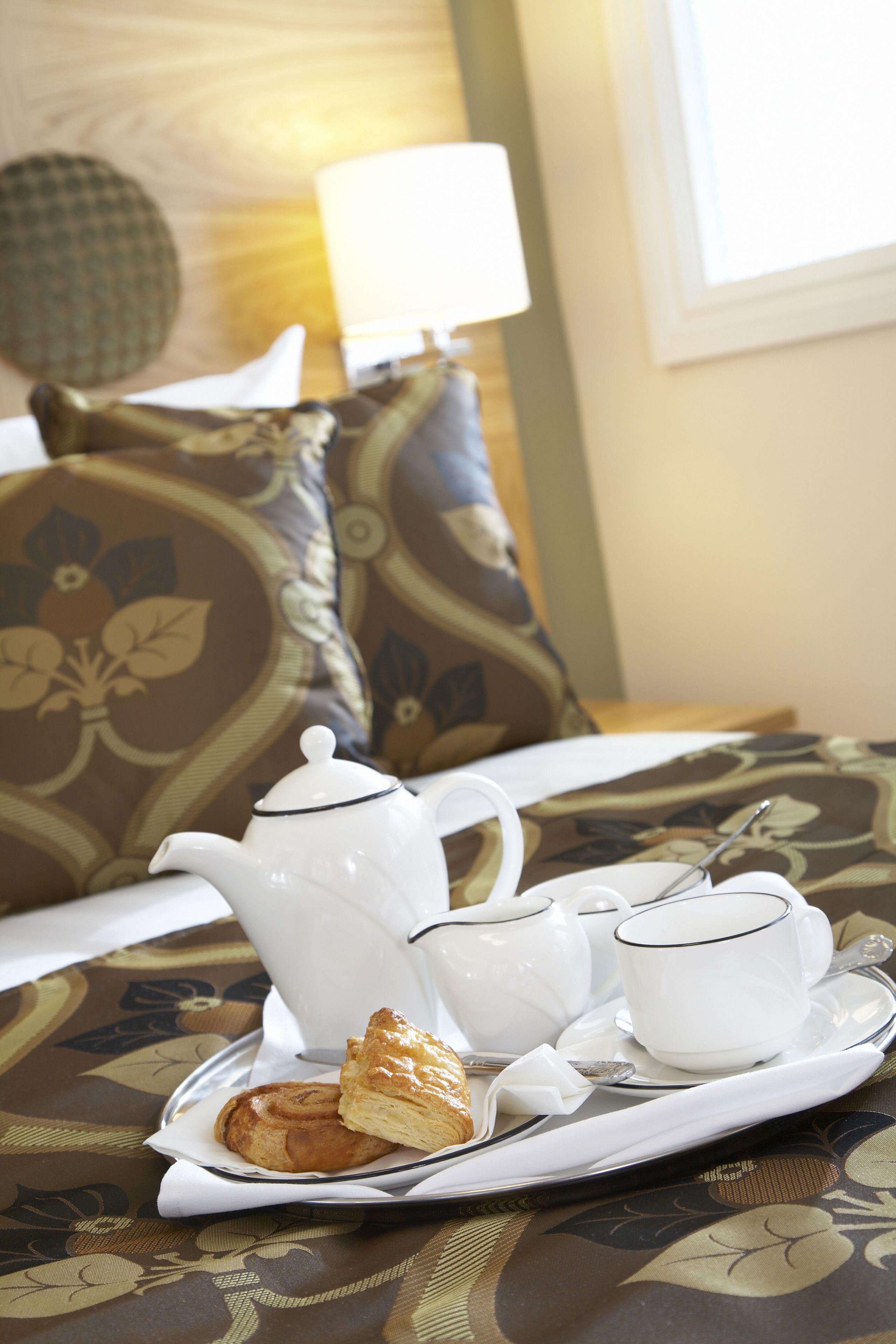A tray with a teapot, cups, and a pastry on a patterned tablecloth.