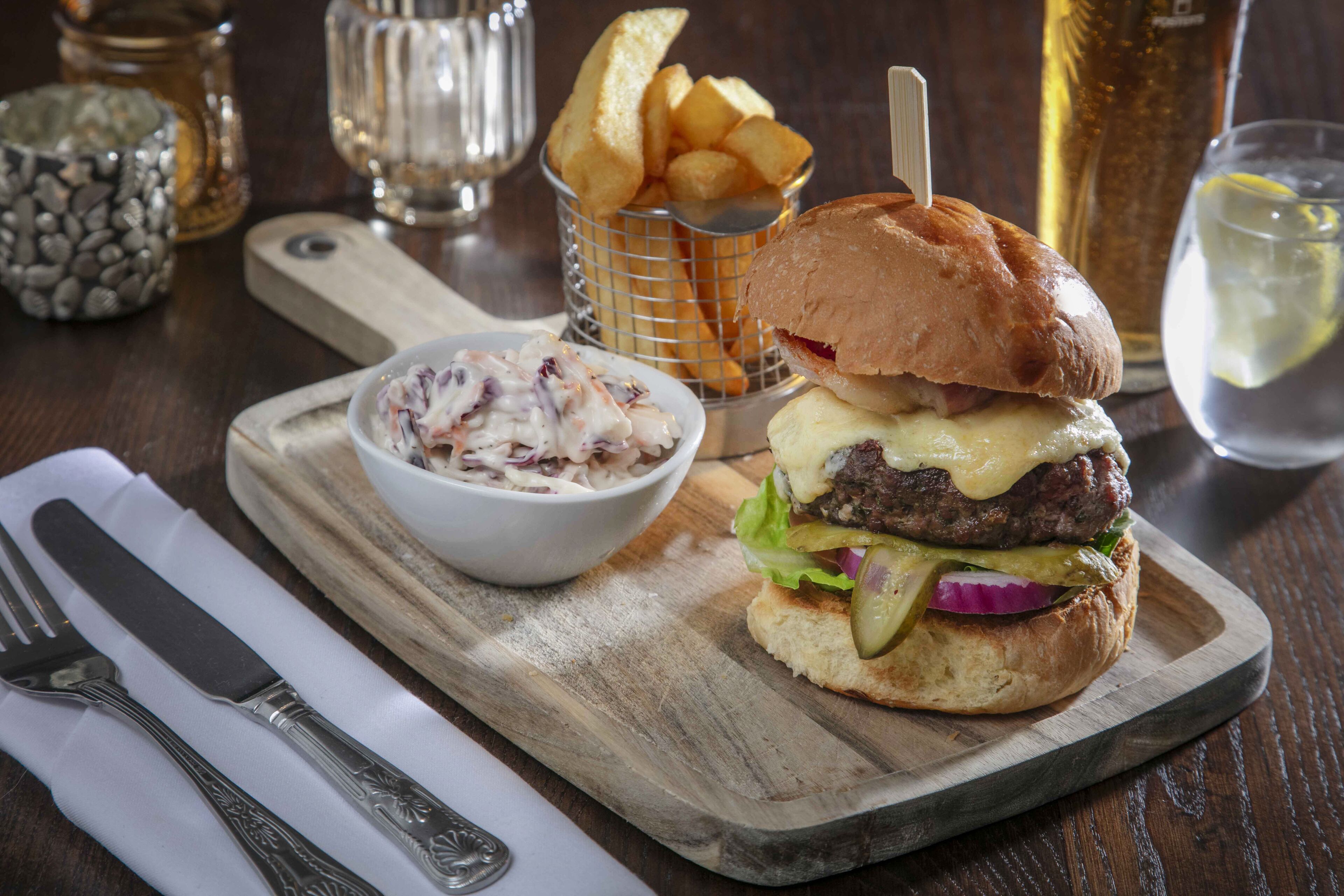 A burger with fries and coleslaw on a wooden board.