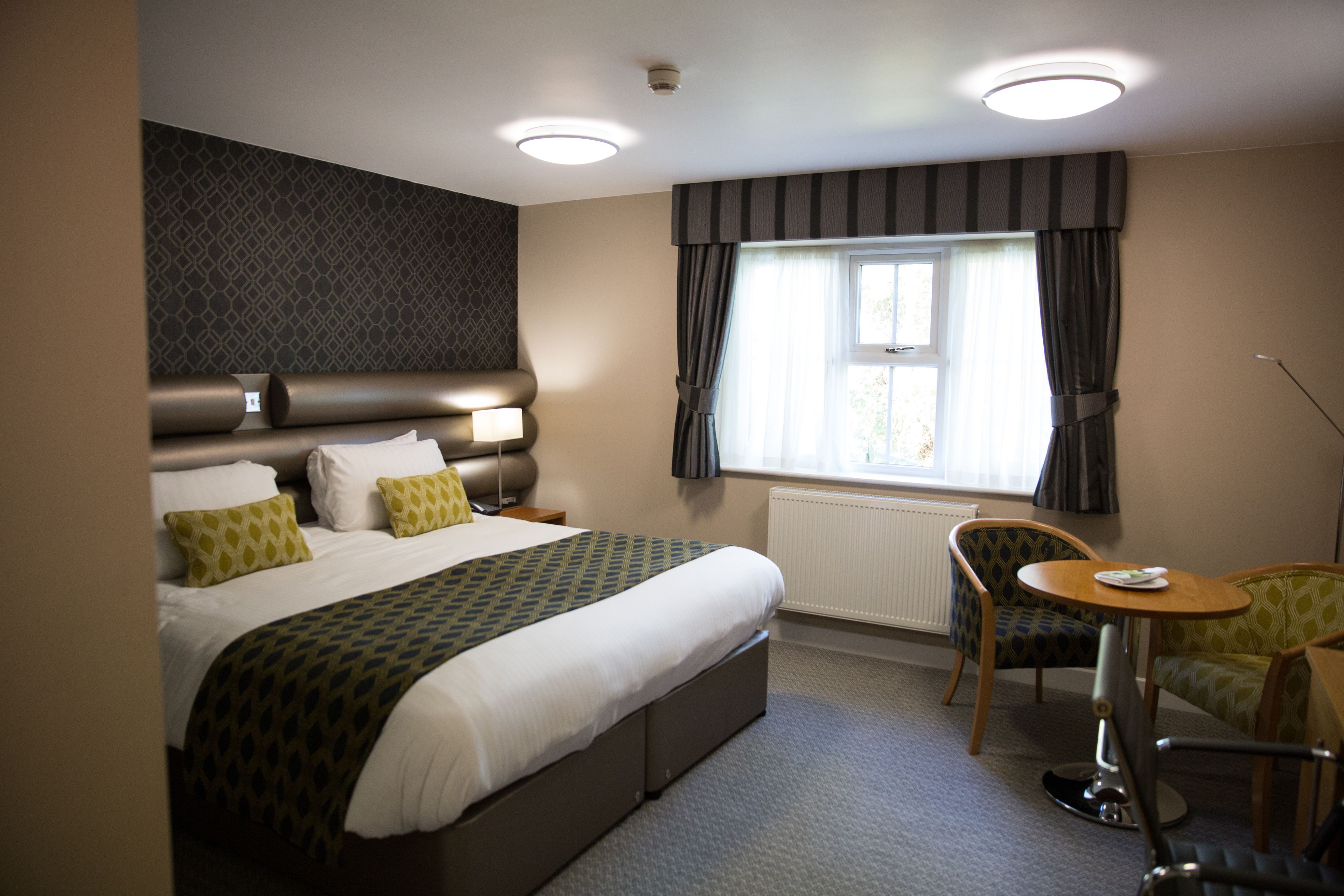 A hotel room with a large bed, bedside lamps, a small table, and a chair.
