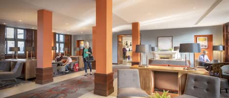 A hotel lobby with seating areas, a reception desk, and a fireplace.