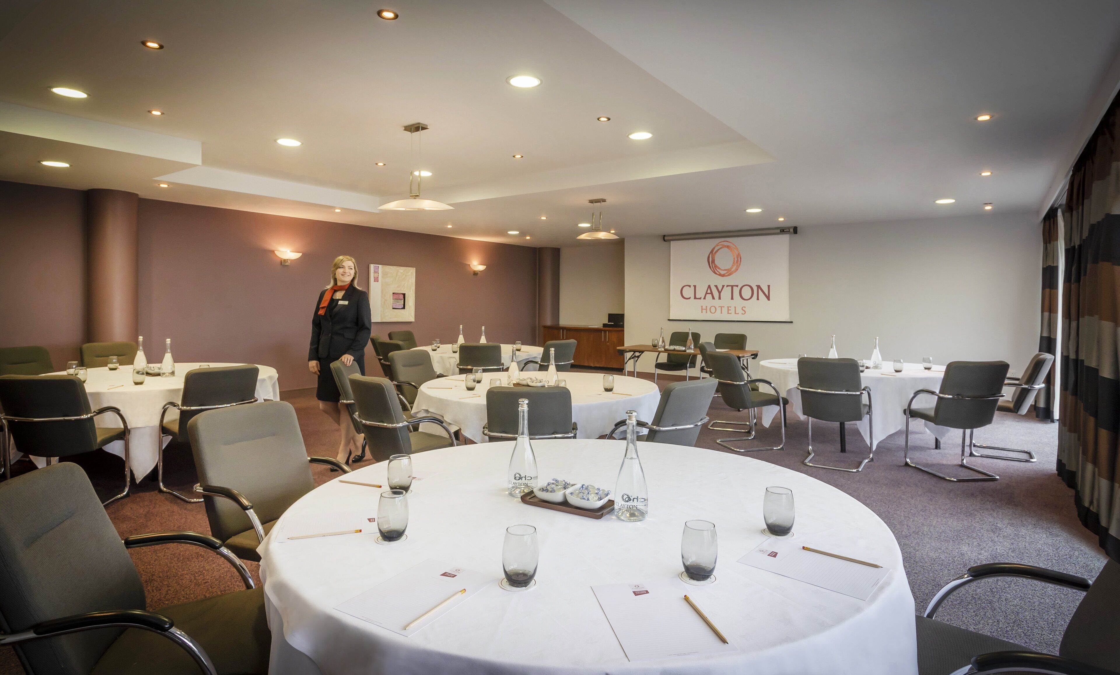 Une salle de conférence équipée de tables rondes, de chaises et d’un écran de présentation affichant le nom « Clayton Hotels ».