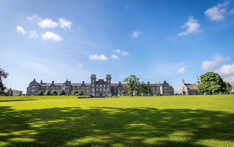 A large, historic building with multiple towers and a spacious lawn in front.