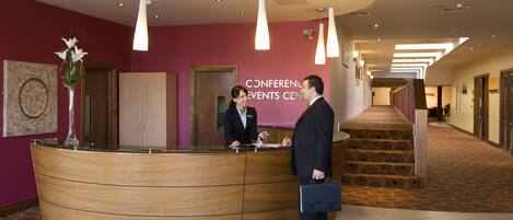 A reception area with a curved wooden desk, a receptionist, and a man with a briefcase.