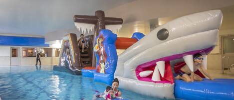 An indoor swimming pool with inflatable play structures, including a shark and a pirate-themed slide.