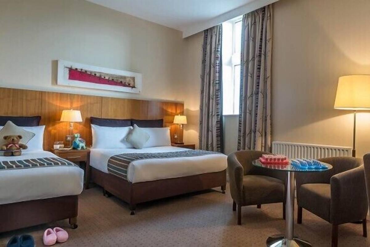A hotel room with two beds, a sitting area with a table, and a window with curtains.
