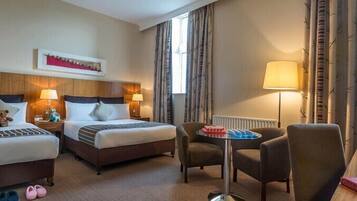 A hotel room with two beds, a sitting area with a table, and a window with curtains.