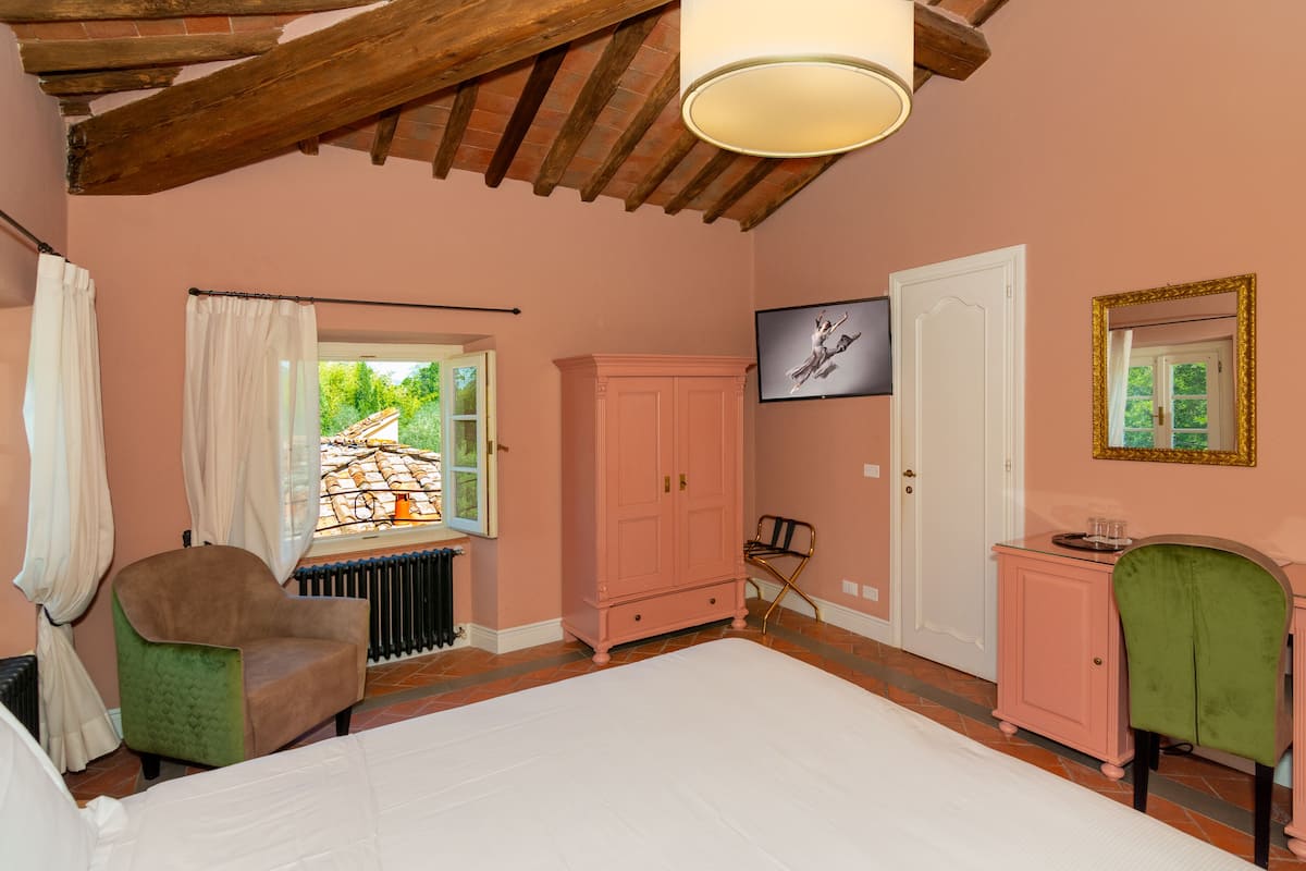 A bedroom with a bed, a window with curtains, a radiator, a wardrobe, a television, and a mirror.