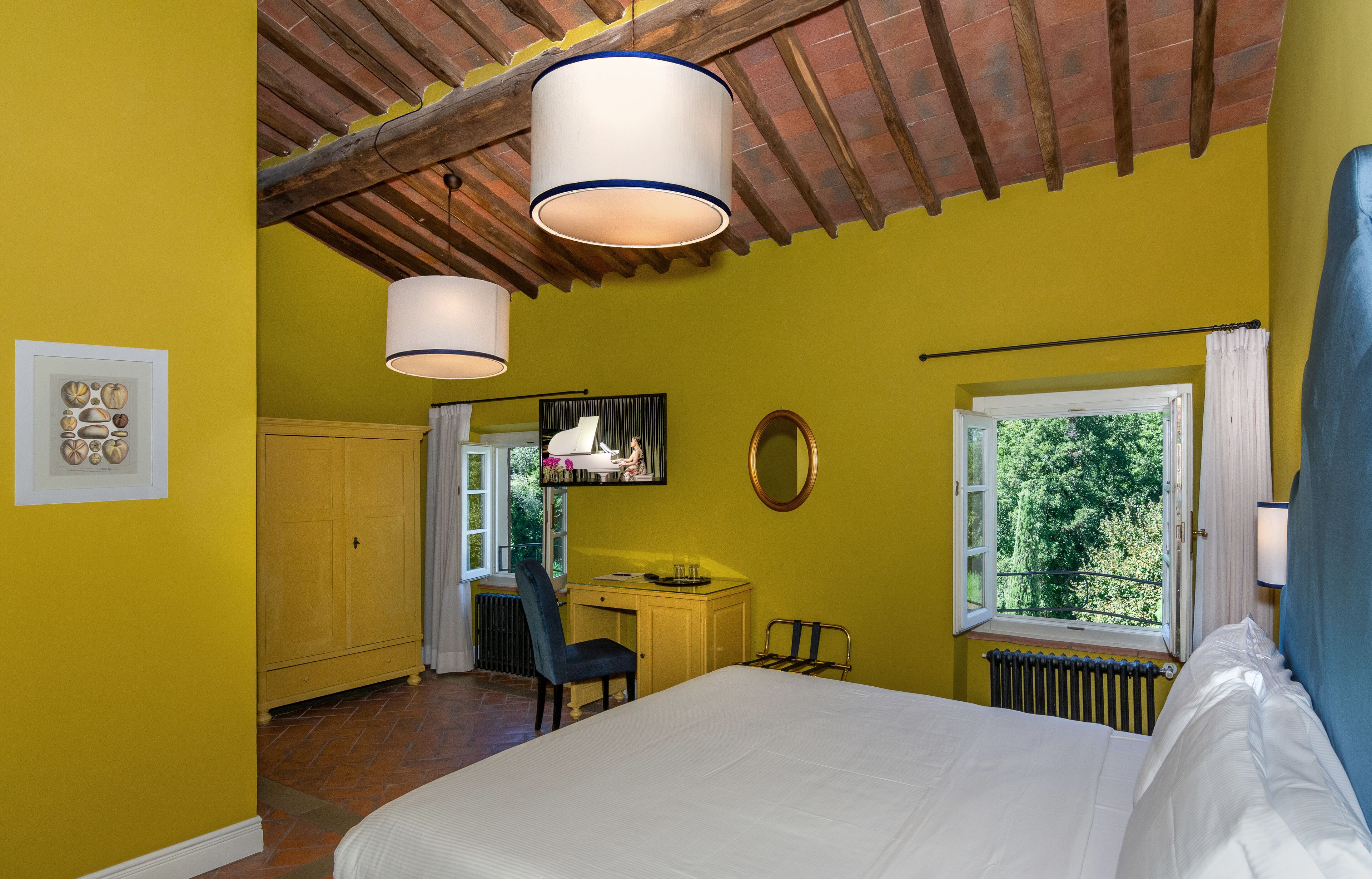 A bedroom with a bed, a desk, a chair, a radiator, a window with a view, and a ceiling with exposed beams.