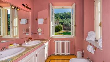 Un bagno rosa con due lavandini, un water e una finestra che si affaccia sul verde.