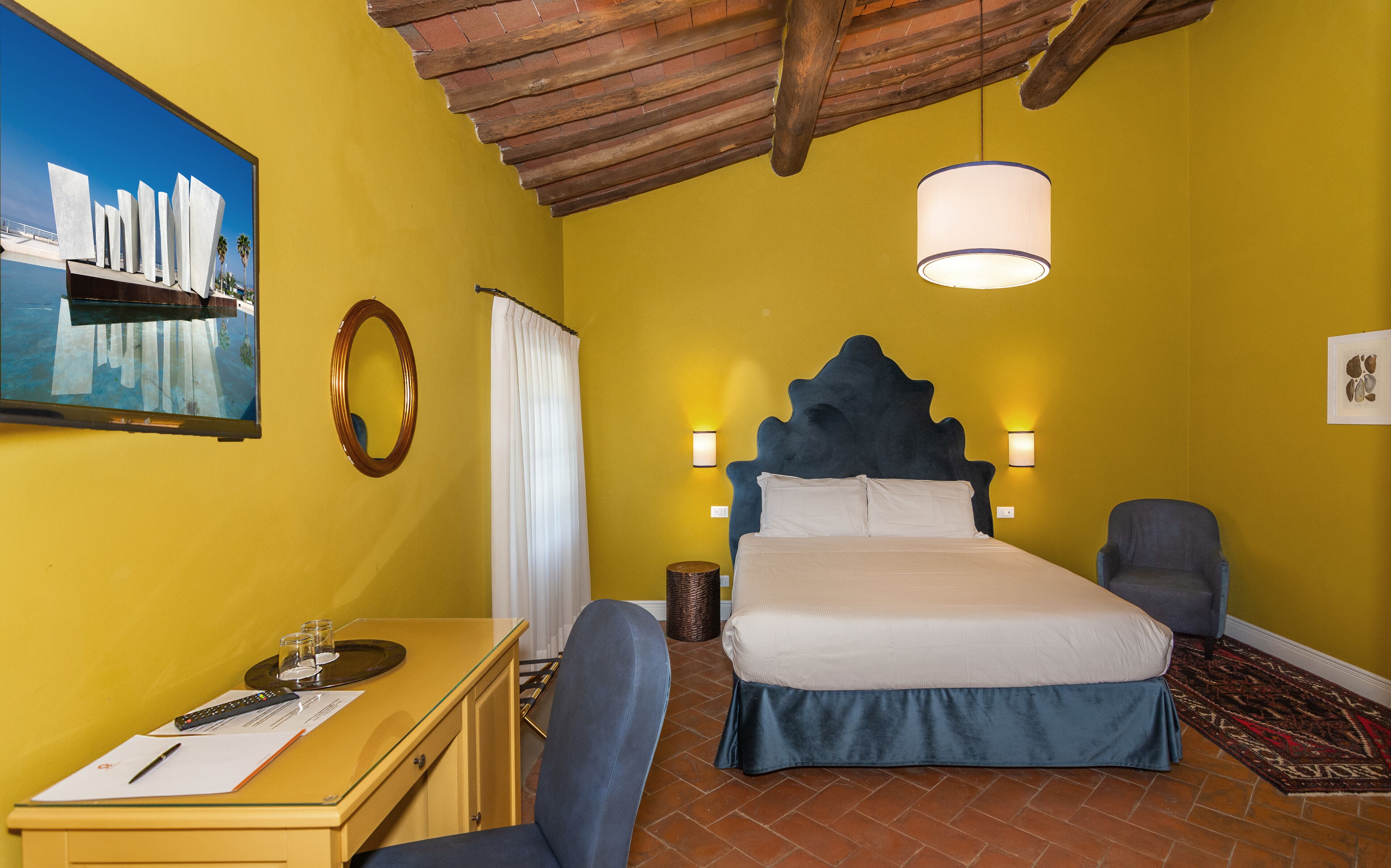 Ein Hotelzimmer mit einem Bett, zwei Sesseln, einem Schreibtisch mit Lampe, einem Spiegel und einem Bild an der Wand.