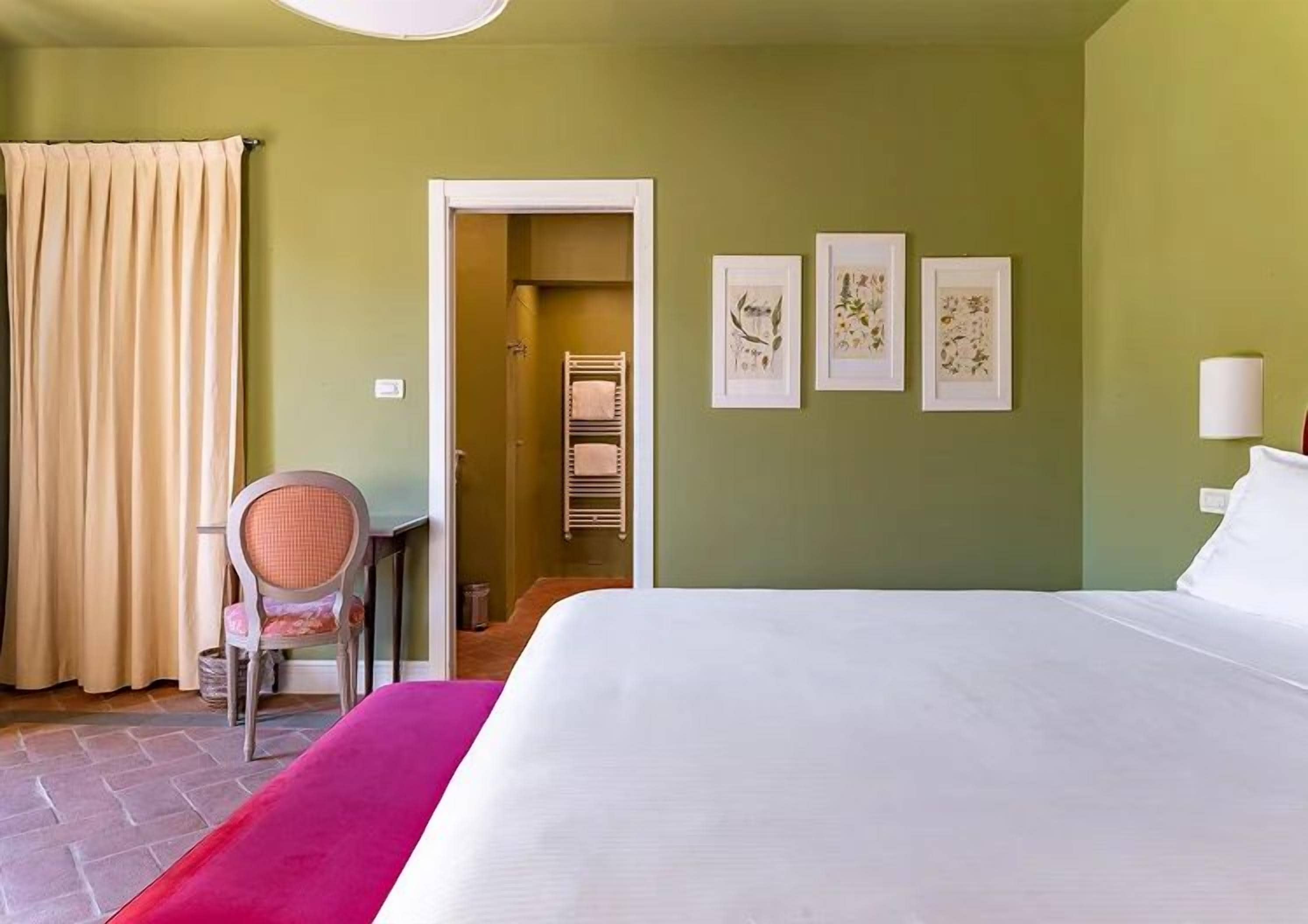 Een hotelkamer met een bed, een stoel, een deur naar een badkamer en drie ingelijste foto's aan de muur.