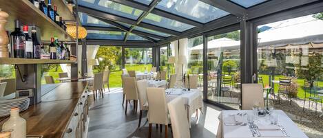 A restaurant with a glass roof, tables set for dining, and wine bottles on shelves.
