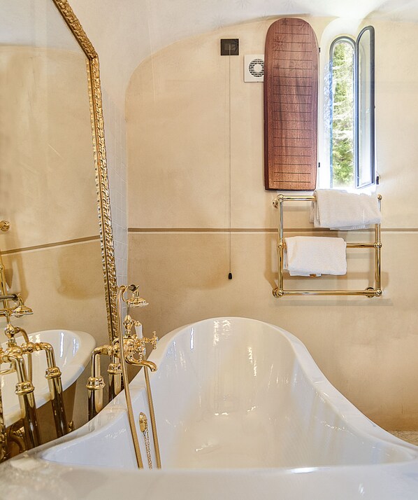 Un baño lujoso con una bañera independiente, grifería dorada y una puerta de madera.