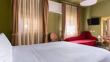 Une chambre d’hôtel avec un grand lit, un fauteuil rouge, un bureau avec une lampe et des rideaux.