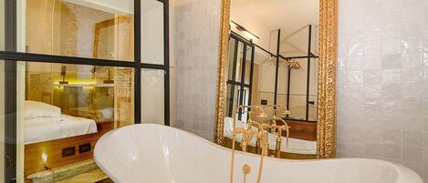 A bathroom with a large bathtub, a mirror with a gold frame, and a shower area.