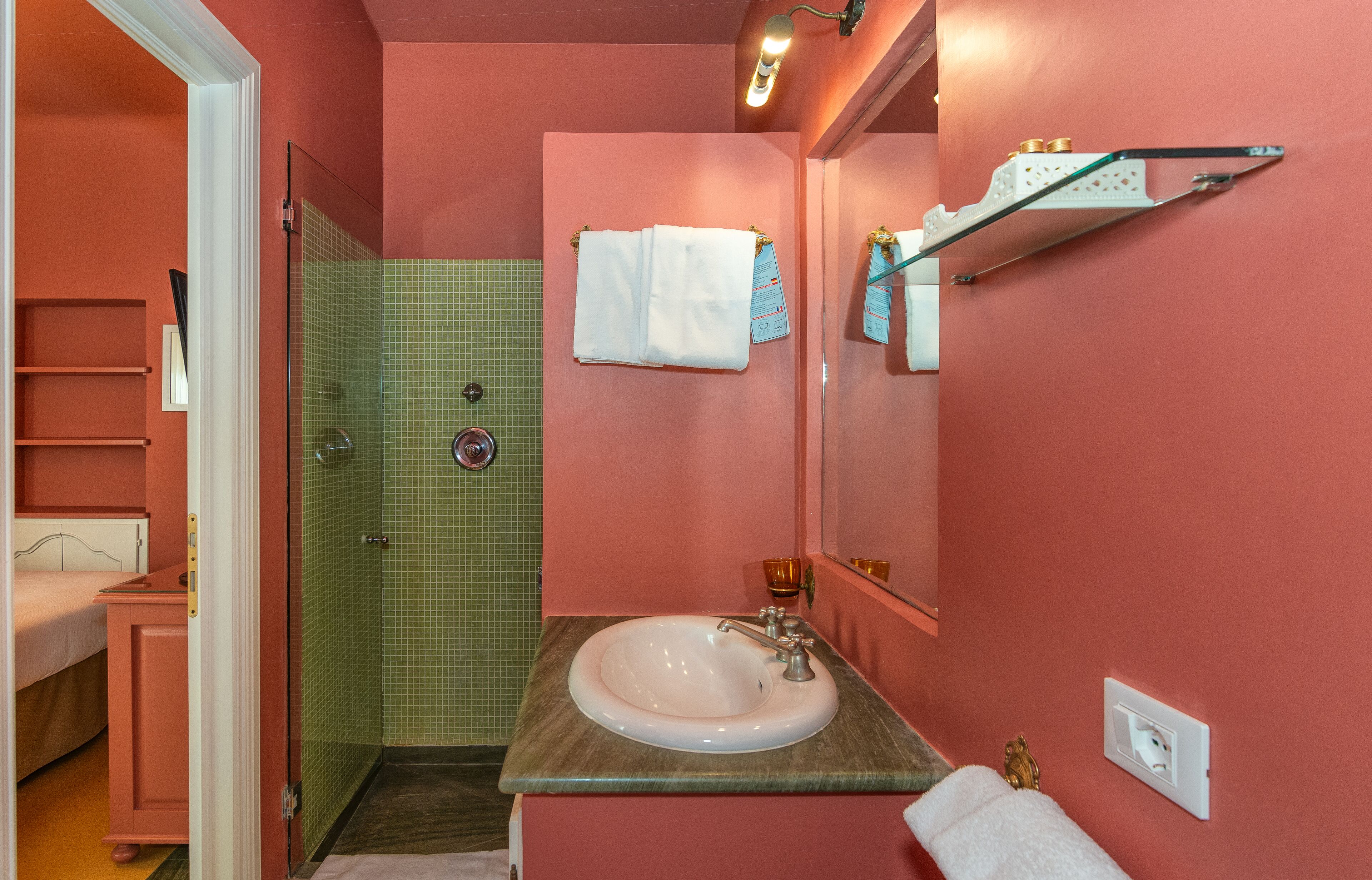 A bathroom with a pink wall, a glass shower enclosure, a sink, and a mirror.