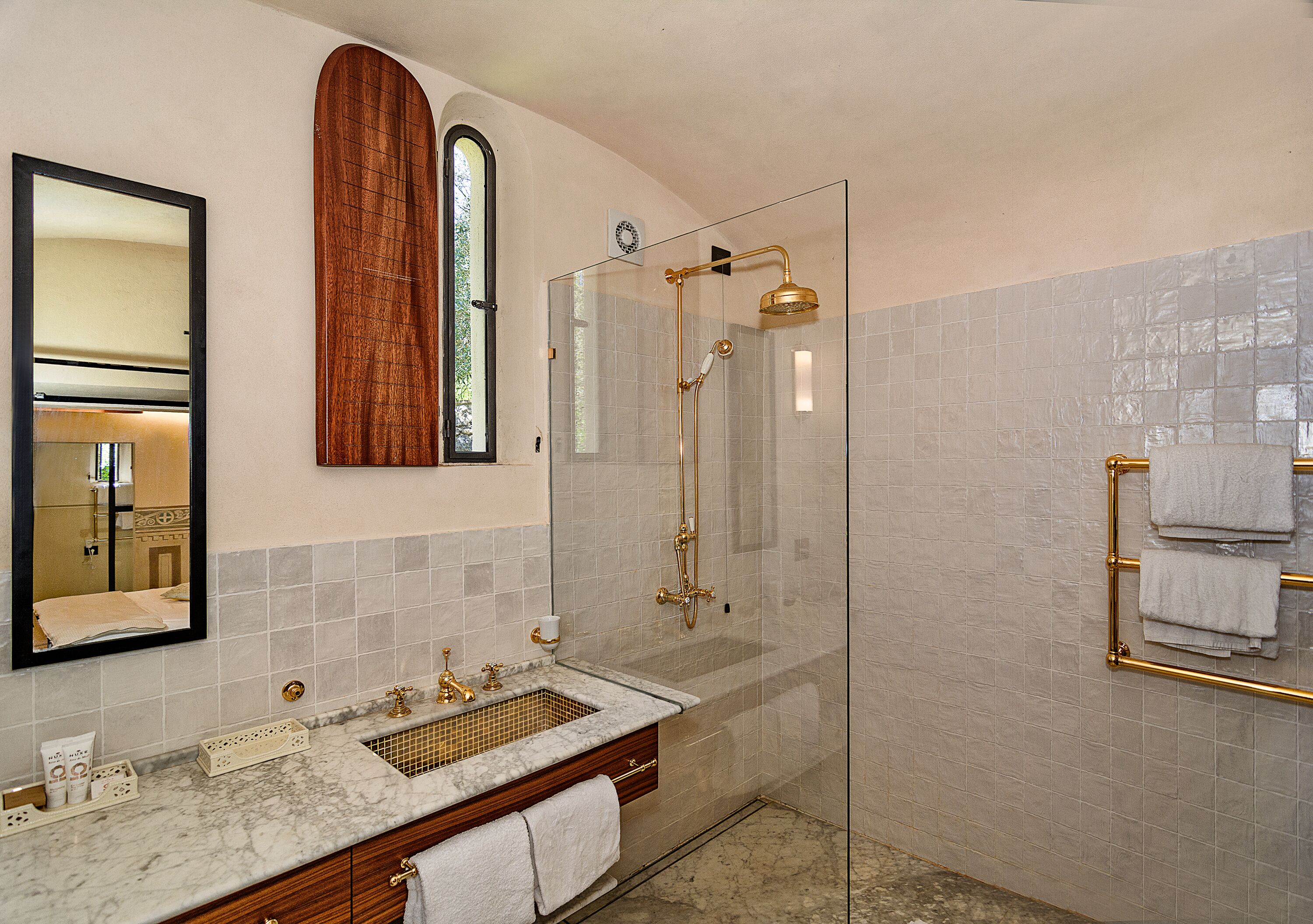 Un baño con lavamanos de mármol, ducha con cerramiento de vidrio y tocador de madera.
