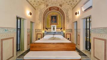 Una cama grande, ubicada en el centro, con cabecera de madera, flanqueada por dos puertas a cada lado.