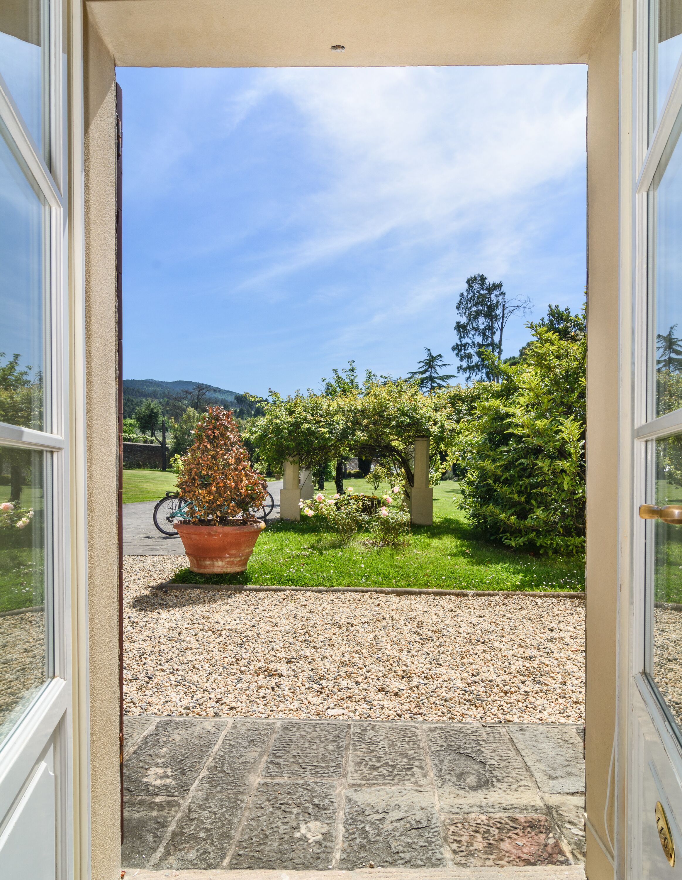 A doorway leading to a garden with a gravel path, a potted plant, and a bicycle.
