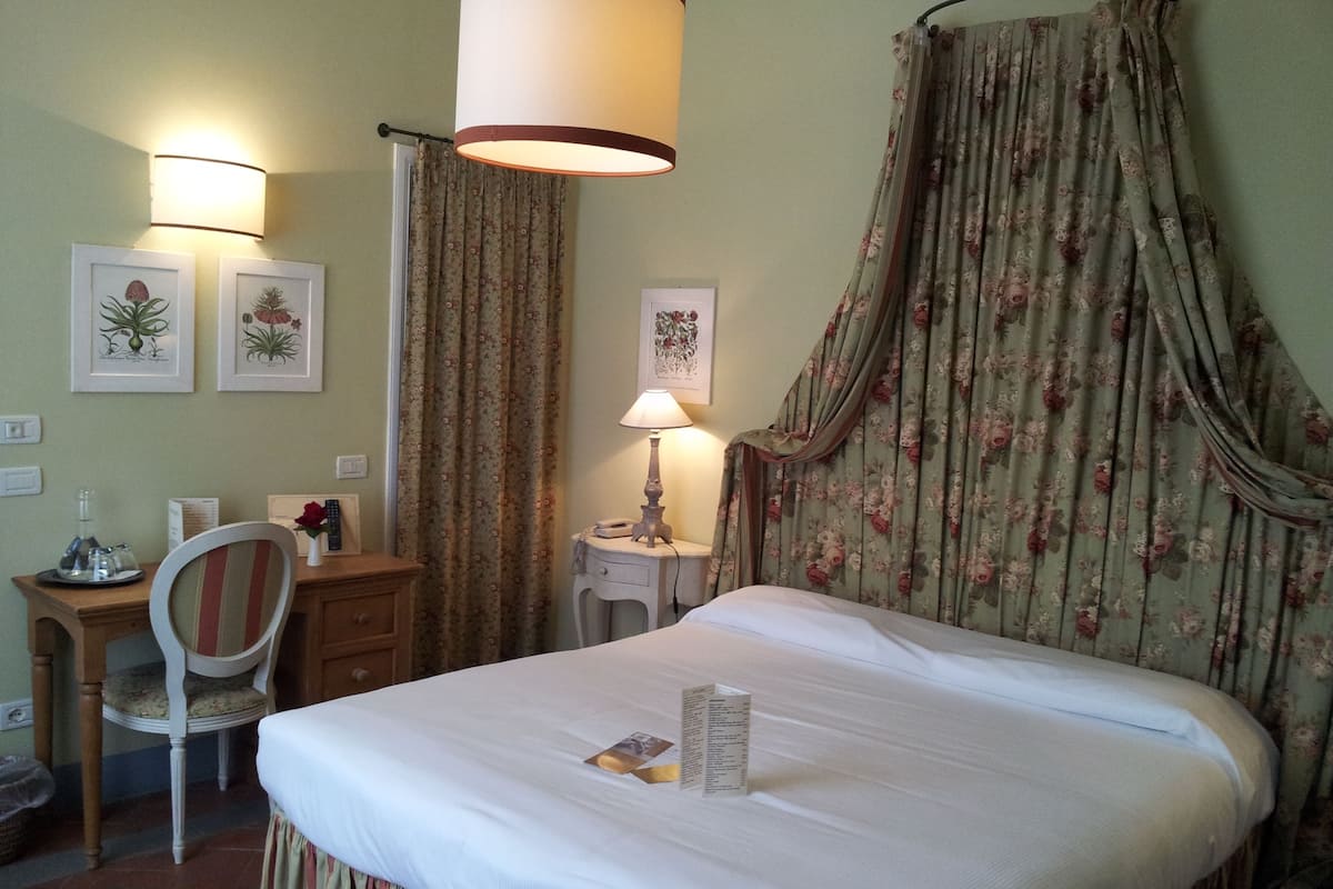 A neatly arranged hotel room with a bed, a desk, a chair, and a lamp.