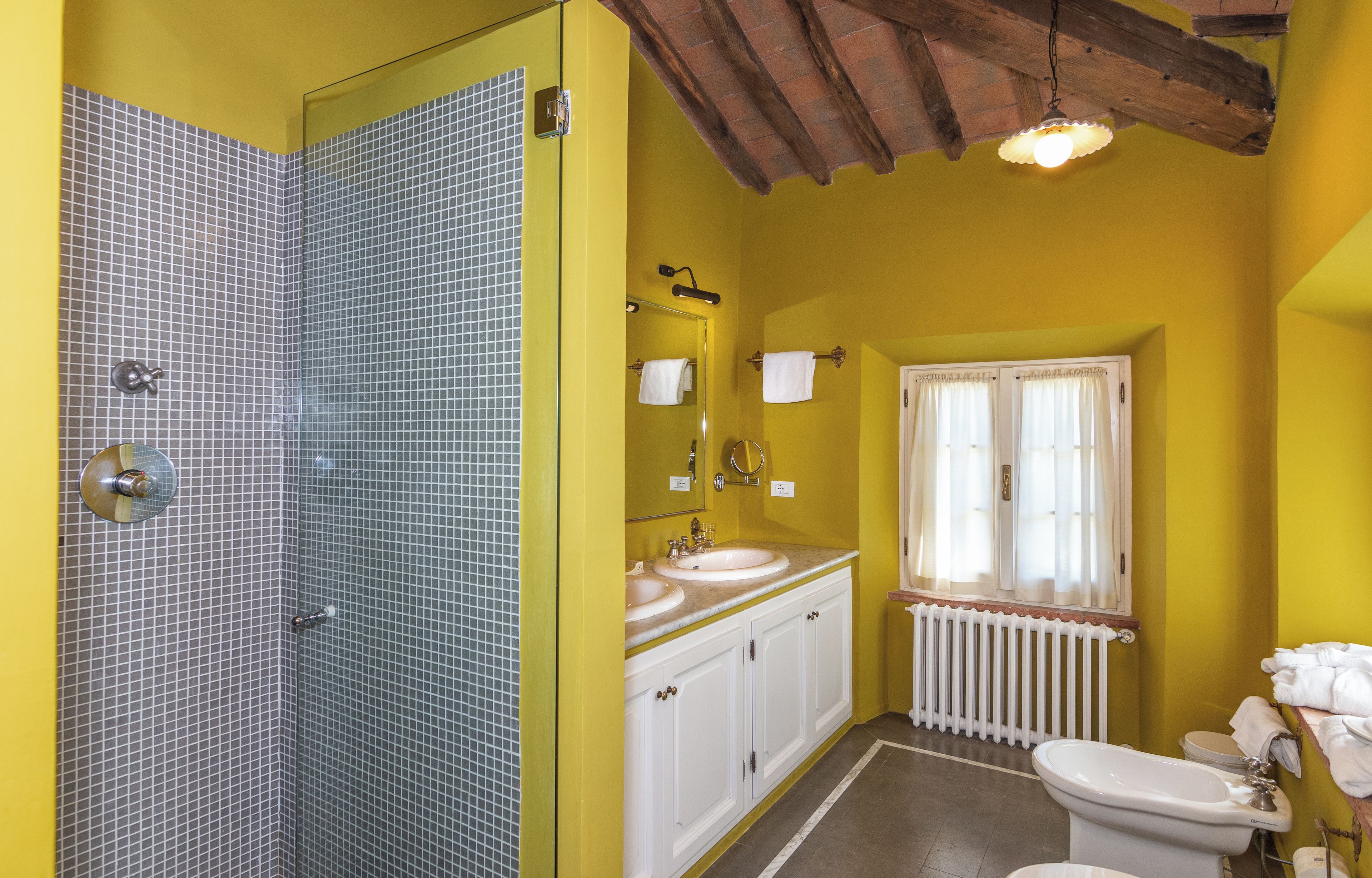 Un baño con ducha, lavamanos, inodoro y una ventana con cortinas.