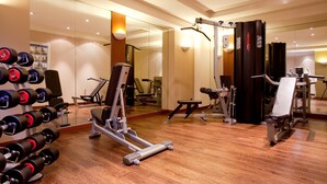 Une salle de sport équipée de divers appareils d’exercice, notamment des haltères, un banc de développé couché et un tapis de course.