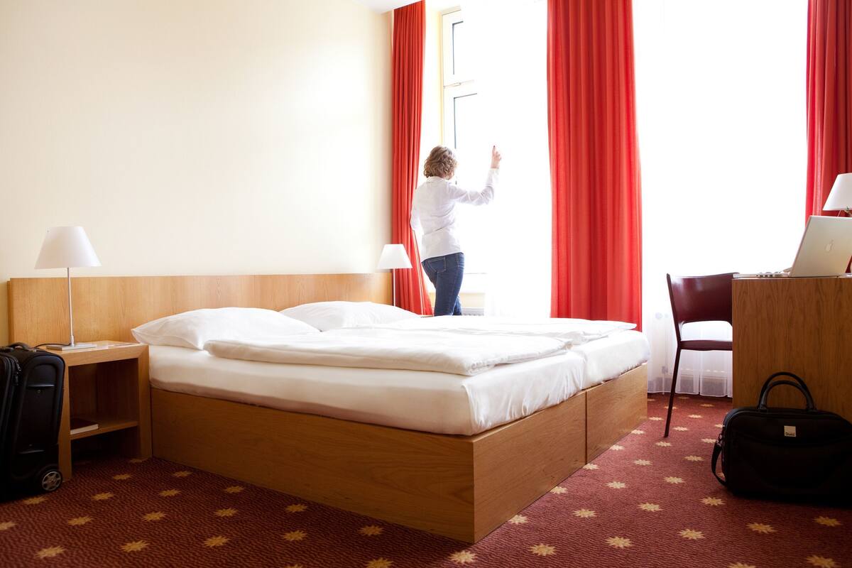 Ein Hotelzimmer mit einem hölzernen Bett, einem Schreibtisch mit einem Laptop, einem Sessel und einem Koffer.