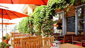 Un café en plein air avec des tables et des chaises en bois, des parasols rouges et des plantes en pot.